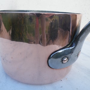 May include: A copper saucepan with a black iron handle. The saucepan has a shiny, reflective surface.