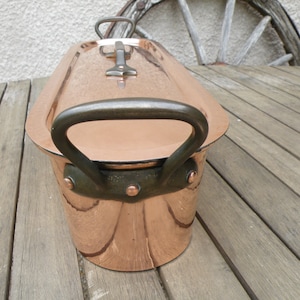 May include: An oval copper roasting dish with two handles on the sides and one handle on the lid. The dish has a shiny, polished finish.