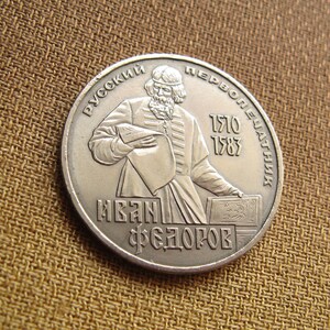 May include: Silver coin featuring a portrait of Ivan Fedorov, the first Russian printer, with the text "РУССКИЙ ПЕРВОПЕЧАТНИК" (Russian First Printer) and "ИВАН ФЕДОРОВ" (Ivan Fedorov) surrounding the portrait. The dates "1510" and "1583" are also visible.