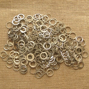 Könnte beinhalten: Ein großer Haufen silberner Metallringe auf einem braunen Jutesack-Hintergrund.