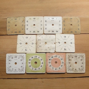 Pode incluir: Dez mostradores de relógio vintage com números e ponteiros pretos. Os mostradores dos relógios são brancos com números e ponteiros pretos. Alguns dos mostradores dos relógios têm uma borda decorativa. Os mostradores dos relógios são de vários tamanhos e formas.