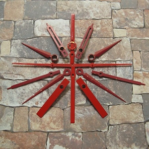 May include: A set of red clock hands, including hour, minute, and second hands, arranged in a starburst pattern on a stone background.