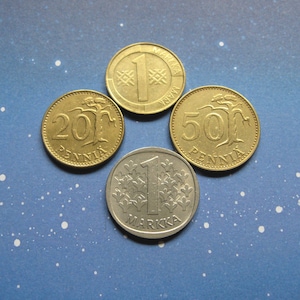 May include: Four Finnish coins, one silver and three gold, on a blue background with white dots. The coins are 1 Markka, 20 Pennia, 50 Pennia, and 1 Markka.