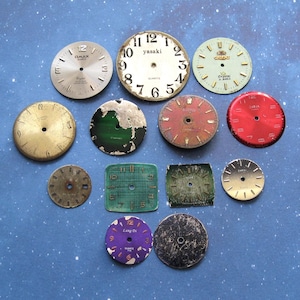 Puede incluir: Una colección de esferas de reloj vintage de varias formas y tamaños. Las esferas incluyen formas redondas, cuadradas e irregulares, con colores que van del dorado y plateado al rojo y verde. Algunas esferas tienen texto visible, incluyendo "yasaki" y "DMAX".