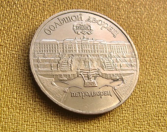 May include: A silver coin featuring a depiction of a building with the text "Большой Дворец" (meaning "Grand Palace") and "Петродворец" (meaning "Peterhof") in Cyrillic script.