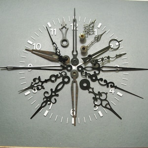 May include: A set of clock hands in various styles and sizes, arranged in a starburst pattern on a grey background. The hands are black metal and have a variety of decorative details.