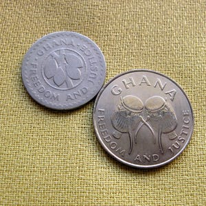 May include: Two silver Ghanaian coins with the words "Freedom and Justice" and the country's name "Ghana" inscribed around the edges. One coin features a stylized flower, while the other depicts two drums.