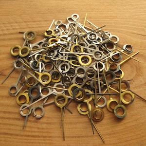 May include: A large pile of gold and silver clock hands. The hands are all different lengths and have different sized holes at the end.