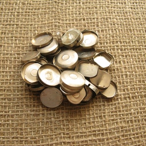 Puede incluir: Un montón de fondos de caja de reloj de metal plateado sobre un fondo de arpillera.