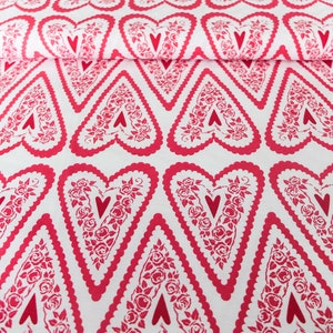 Könnte beinhalten: Weißer Stoff mit einem sich wiederholenden Muster aus rosa Herzen. Jedes Herz hat ein kleineres rosa Herz in der Mitte und ist von einem floralen Design umgeben.