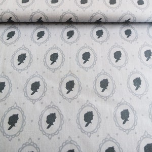 Könnte beinhalten: Ein weißer Stoff mit einem sich wiederholenden Muster aus schwarzen Silhouetten von Menschenköpfen in ovalen Rahmen. Die Rahmen haben ein dekoratives Design.