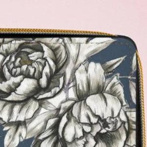 K&ouml;nnte beinhalten: Nahaufnahme einer dunkelblauen Geldb&ouml;rse mit goldenem Rei&szlig;verschluss und floralem Design. Das Design zeigt gro&szlig;e, detaillierte wei&szlig;e und graue Pfingstrosenbl&uuml;ten und -bl&auml;tter. Die Geldb&ouml;rse befindet sich auf einem rosa Hintergrund.