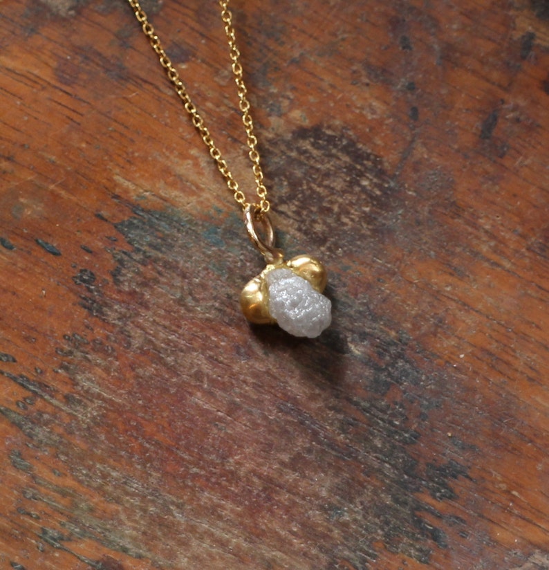 May include: A gold chain necklace with a raw diamond pendant. The diamond is a light gray color and has a rough, natural texture.