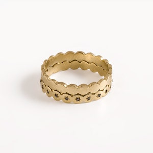 May include: A gold ring with a scalloped edge and black diamonds. The ring is made of two bands that are stacked on top of each other.