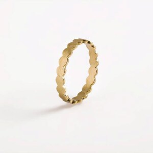 May include: A gold ring with a scalloped edge. The ring is made of a series of small, round shapes.