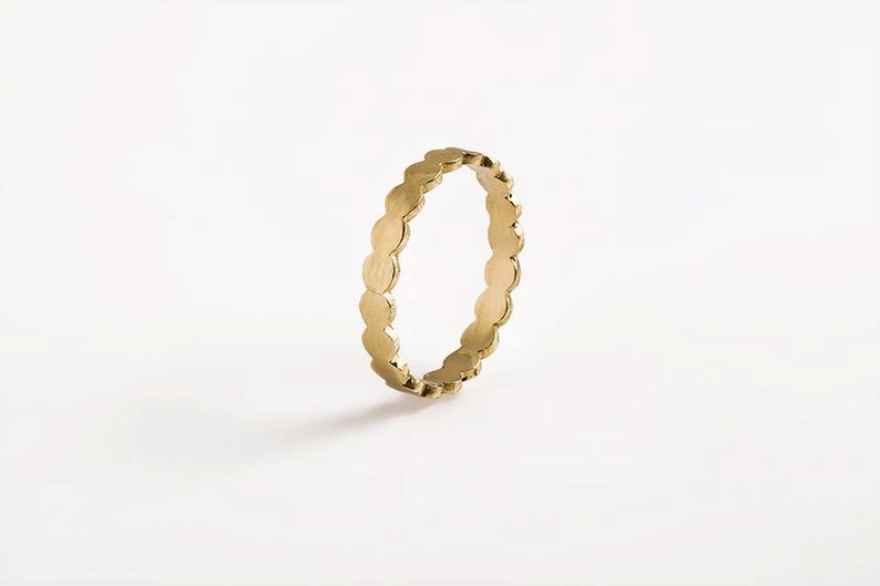 May include: A gold ring with a scalloped edge. The ring is made of a series of small, round shapes.
