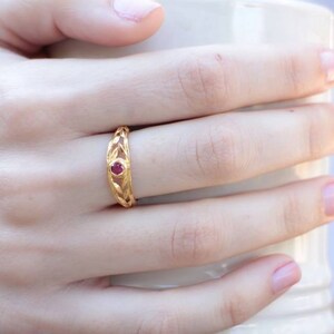 May include: A gold ring with a delicate, intricate design featuring a single red gemstone in the center.