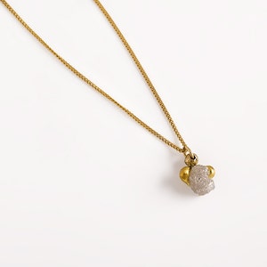 May include: A gold chain necklace with a pendant made of a rough, gray stone with two gold accents.