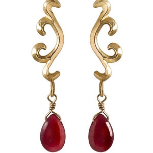 May include: Gold earrings with a delicate, swirling design and dangling red gemstone drops.