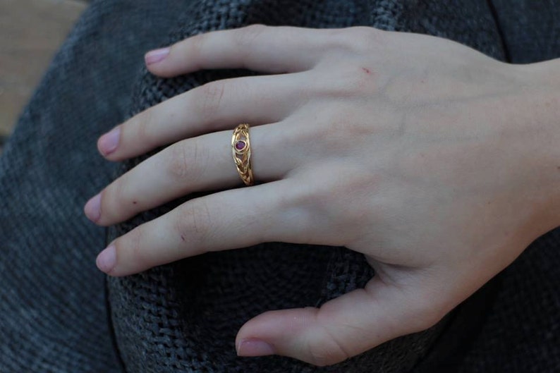 May include: A gold ring with a red gemstone set in the center. The ring has a braided design.