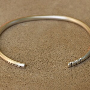 Pu&ograve; includere: Un braccialetto rigido in argento con un design testurizzato su un lato. Il braccialetto &egrave; aperto e ha uno stile semplice e minimalista.