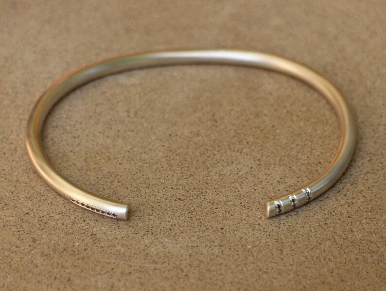 Pu&ograve; includere: Un braccialetto rigido in argento con un design testurizzato su un lato. Il braccialetto &egrave; aperto e ha uno stile semplice e minimalista.