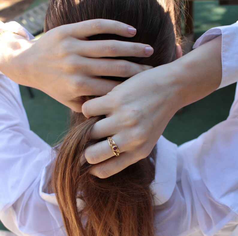May include: A gold ring with a red stone set in a chain-link design.
