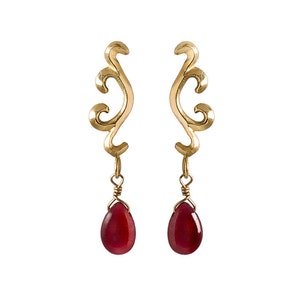 May include: Gold earrings with a delicate, swirling design and dangling red teardrop-shaped stones.