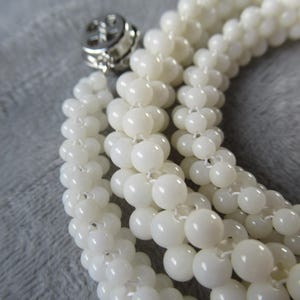 May include: A white pearl necklace with a silver clasp. The necklace is made of multiple strands of pearls, creating a layered effect.