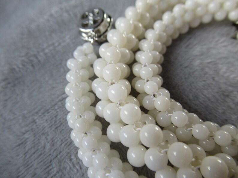 May include: A white pearl necklace with a silver clasp. The necklace is made of multiple strands of pearls, creating a layered effect.