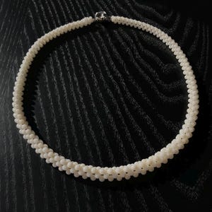 May include: A white pearl necklace with a silver clasp. The necklace is made of small, round pearls that are strung together in a single strand.