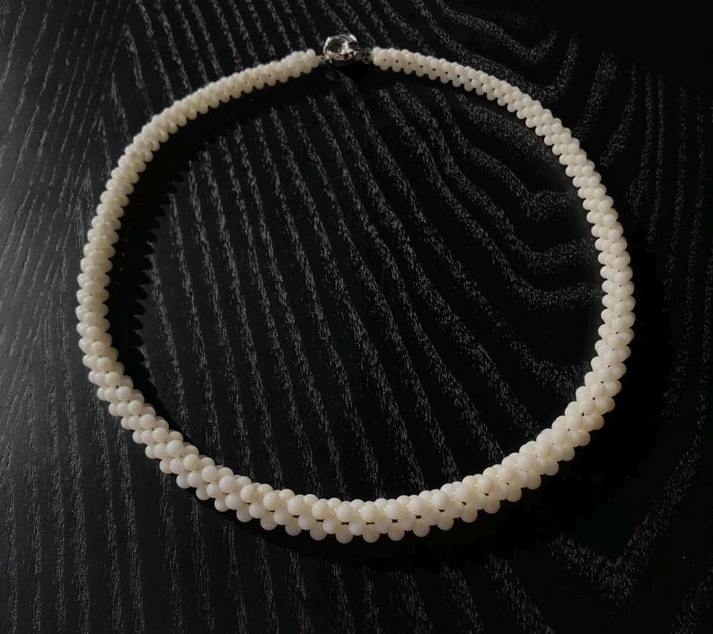 May include: A white pearl necklace with a silver clasp. The necklace is made of small, round pearls that are strung together in a single strand.