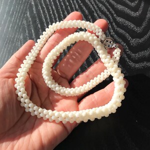 May include: A white pearl necklace and bracelet set. The necklace is longer than the bracelet and both are made of small, round pearls.