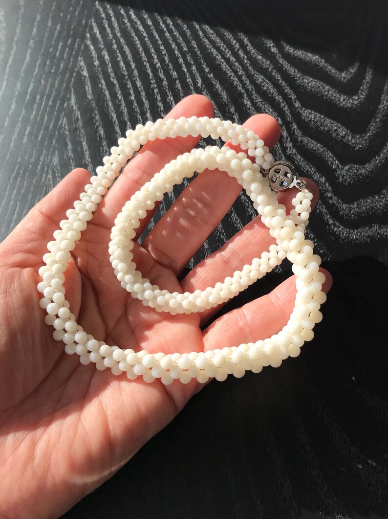 May include: A white pearl necklace and bracelet set. The necklace is longer than the bracelet and both are made of small, round pearls.