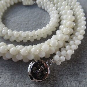 May include: A white beaded necklace with a silver charm. The charm has a design of a four-leaf clover.