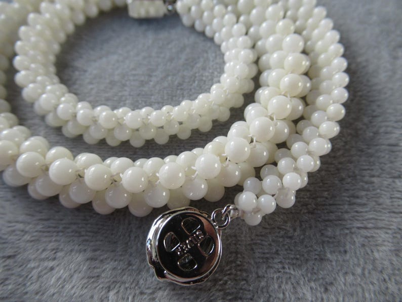 May include: A white beaded necklace with a silver charm. The charm has a design of a four-leaf clover.