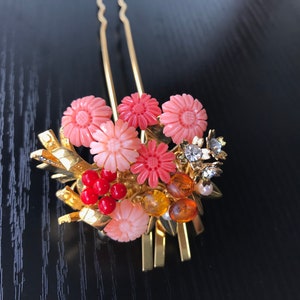 Puede incluir: Un peine de pelo dorado con detalles de flores rosas y naranjas y cuentas rojas. El peine est&aacute; decorado con pedrer&iacute;a y perlas.
