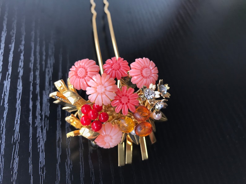 Puede incluir: Un peine de pelo dorado con detalles de flores rosas y naranjas y cuentas rojas. El peine est&aacute; decorado con pedrer&iacute;a y perlas.