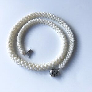 May include: A white pearl necklace with a silver clasp. The necklace is made of small, round pearls and is layered in a triple strand.