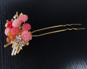 Puede incluir: Una horquilla de pelo dorada con un grupo de flores rosas y rojas, cuentas de ámbar y diamantes de imitación.