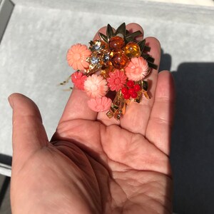 Puede incluir: Un peine de pelo dorado con un racimo de flores de color coral y cuentas de color &aacute;mbar. El peine est&aacute; decorado con hojas doradas y algunas piedras de imitaci&oacute;n transparentes.