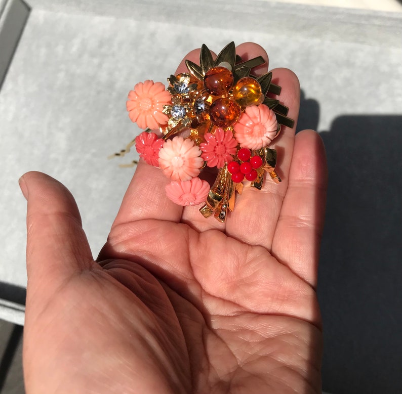 Puede incluir: Un peine de pelo dorado con un racimo de flores de color coral y cuentas de color &aacute;mbar. El peine est&aacute; decorado con hojas doradas y algunas piedras de imitaci&oacute;n transparentes.
