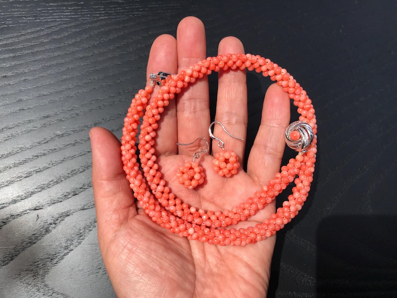 Op de afbeelding: Een zalmkleurige kralenketting en een bijpassend paar oorbellen. De ketting is gemaakt van kleine, getextureerde bolvormige kralen die in een doorlopende streng zijn gerangschikt, vastgezet met een zilverkleurige ronde sluiting met een centrale kraal.