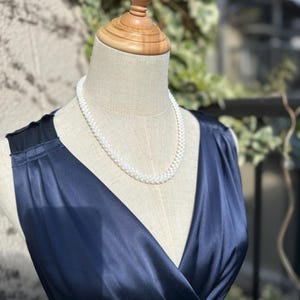 May include: A white pearl necklace on a navy blue satin dress form.