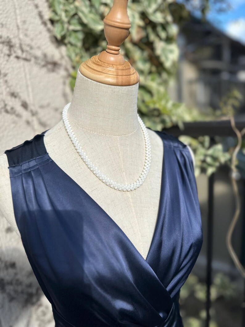 May include: A white pearl necklace on a navy blue satin dress form.