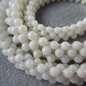 May include: A strand of white round beads made from mother of pearl. The beads are strung on a white thread.