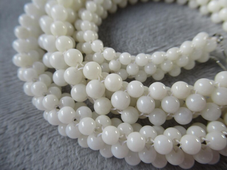 May include: A strand of white round beads made from mother of pearl. The beads are strung on a white thread.