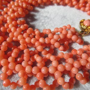 Puede incluir: Primer plano de un collar de cuentas de coral. El collar presenta m&uacute;ltiples hilos de peque&ntilde;as cuentas redondas de color melocot&oacute;n. Se ve un cierre dorado con una piedra de color melocot&oacute;n. Las cuentas son de tama&ntilde;o uniforme y est&aacute;n bien ensartadas.