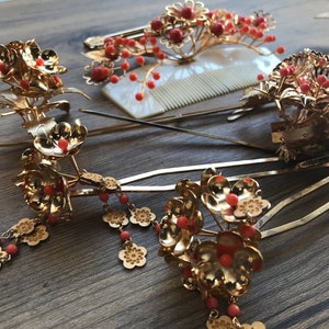 Op de afbeelding: Een set van zes gouden haar kammen met rode bloemen accenten. De kammen zijn versierd met kleine rode kralen en hebben een delicaat bloemenpatroon.