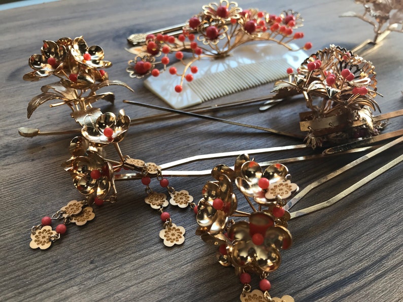 Op de afbeelding: Een set van zes gouden haar kammen met rode bloemen accenten. De kammen zijn versierd met kleine rode kralen en hebben een delicaat bloemenpatroon.
